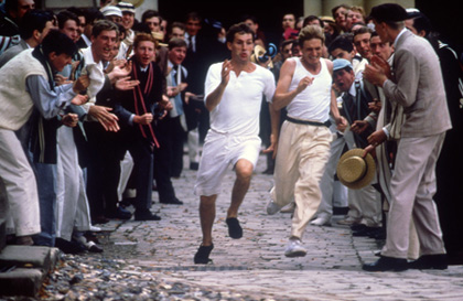 Two young men sprint through a crowd of other men cheering them on