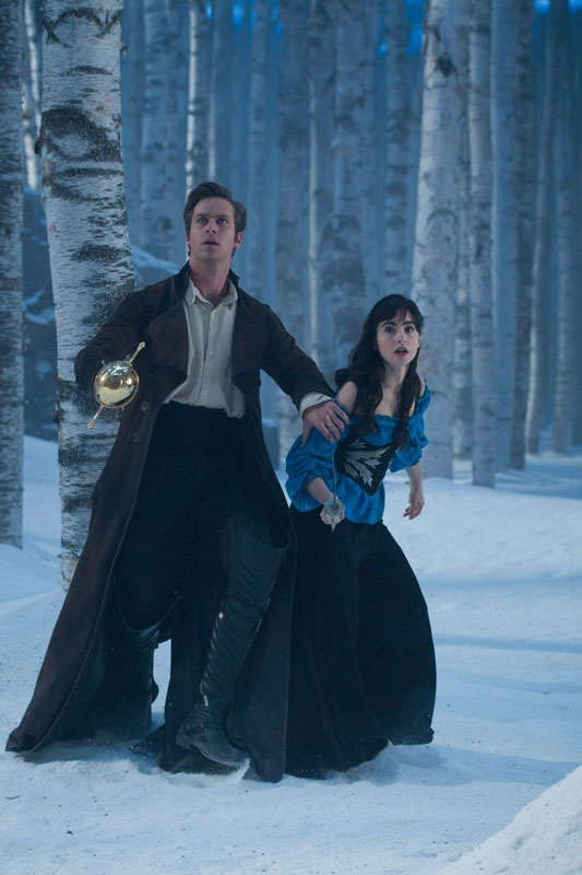 A snowy forest scene at dusk. A man in period dress is brandishing a sword and shielding a young woman, also holding a sword. They are both looking at something out of shot