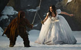A snow scene. A young woman dressed in a white gown is having a sword fight with a dwarf