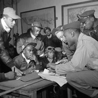 A group of black pilots huddled around a desk looking at maps and talking to each other