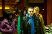 Mid shot of four young women, interior of a cafe, night. The women are dressed in urban clothing and have serious expressions, as though anticipating conflict