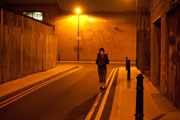 Long shot of a vulnerable looking young girl, in the centre of the shot; exterior, street, night, lit by a street lamp which casts a eerie yellow light over the shot
