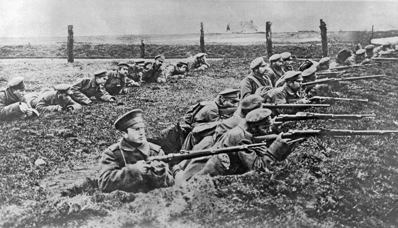 A black and white image of two rows of soldiers from World War One in trenches.  The front row are aiming their rifles at a target out of shot. 