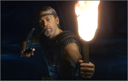 Beowulf thrusts a torch towards the viewer, whist holding his sword ready