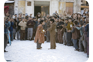 Still image from The Kite Runner - 2 boys face each other in a street, surrounded by a large crowd