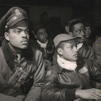 Group of African American airmen in flight jackets and caps listening to someone off camera