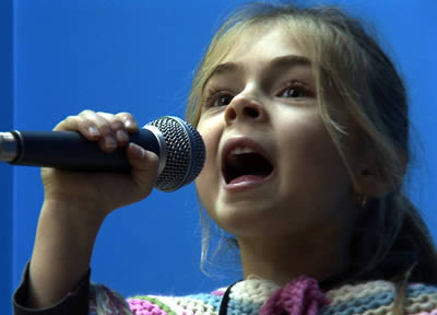 close up shot of a young blonde girl singing into a microphone held close to her mouth
